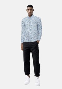 Camicia leggera a maniche lunghe di colore azzurro con motivo floreale, abbinata a pantaloni neri arrotolati e sneakers bianche. Tessuto morbido e vestibilità su misura.