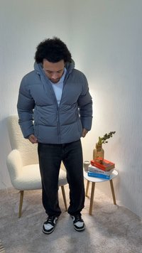 Grå boblejakke med hette, glidelåslukking og sidelommer. Brukt over en hvit skjorte, kombinert med mørke bukser og svarte joggesko.