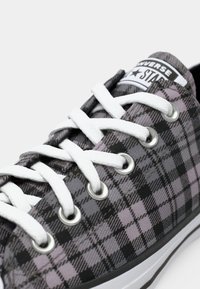 Sneaker in tela a scacchi nera e grigia con lacci bianchi, occhielli in metallo e suola in gomma nera con un bordo bianco a contrasto.