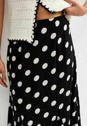 Zwarte rok met grote witte polka dots, gedragen met een witte, gebreide cropped top met zwarte randen en een knoopsluiting.