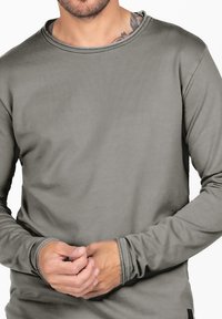 Langärmliges Shirt aus olivgrüner Baumwolle, mit einem runden Halsausschnitt, genähten Akzenten und gerippten Bündchen. Der Stoff wirkt weich mit einer glatten Textur.