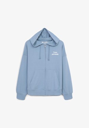 Felpa con zip di colore azzurro chiaro, realizzata in tessuto morbido, con tasca anteriore, lacci e testo stampato di colore bianco sul petto.