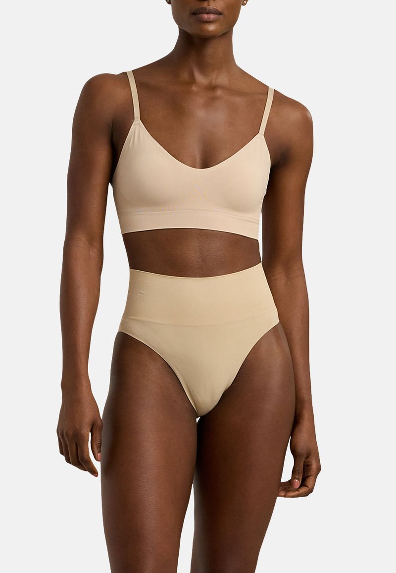 Nude bralette och high-waisted brief-set; sömlös design, mjukt tyg, justerbara band, glansig yta, minimalistisch stil utan synlig hårdvara.