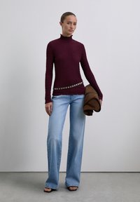 Burgundy textured turtleneck sweater, light wash wide-leg jeans, and a brown jacket with a studded belt. Black open-toed heels.