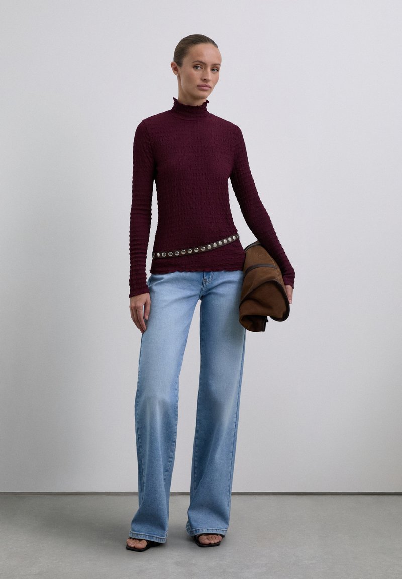 Burgundy textured turtleneck sweater, light wash wide-leg jeans, and a brown jacket with a studded belt. Black open-toed heels.