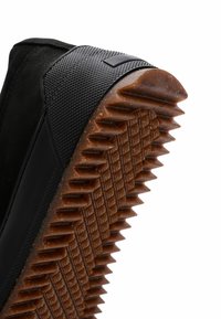 Suela de zapato negra con textura de goma marrón que presenta surcos profundos y angulados, así como un patrón de diamante para mejorar el agarre y la durabilidad.