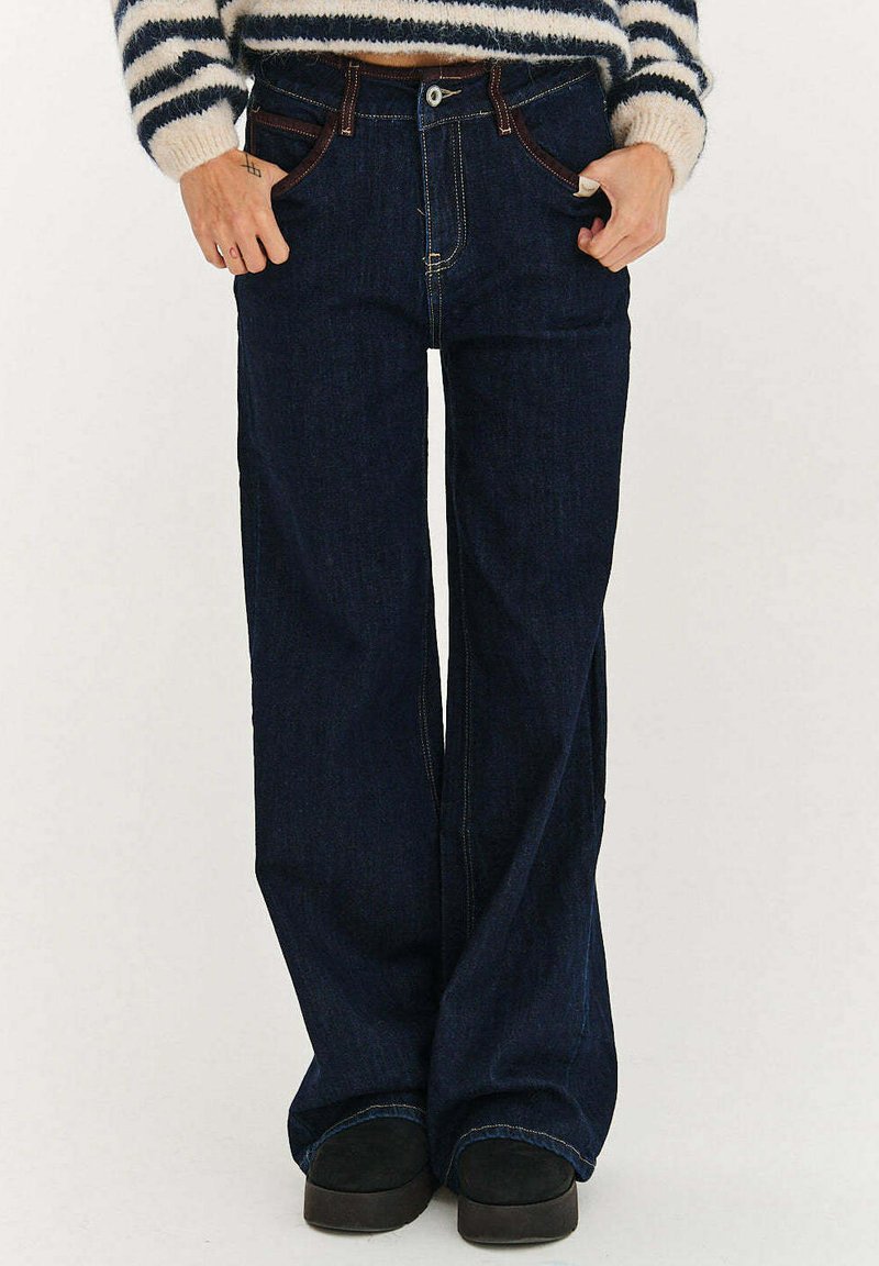 Tmavé džínové kalhoty s širokými nohavicemi a vysokým pasem, zdobené hnělým šitím, předními kapsami a klasickým zapínáním na knoflíky a zip.