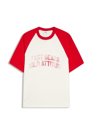 Biały T-shirt z krótkim rękawem, z czerwonymi rękawami raglanowymi i kołnierzem, z wyblakłym czerwonym napisem "FAST BEATS COLD ATTITUDE" z przodu.