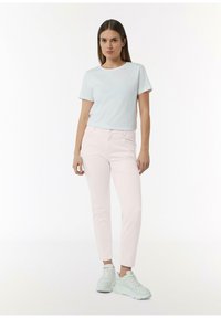 Jasnoniebieska koszulka z krótkim rękawem w połączeniu z różowymi jeansami slim-fit. Teksturowane białe trampki dopełniają stylizację.