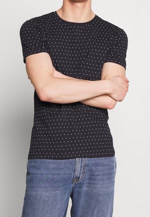 Czarna koszulka z krótkim rękawem z wzorem małych białych trójkątów, wykonana z miękkiego materiału o dopasowanym kroju. Połączona z niebieskimi dżinsami.