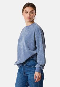 Felpa azzurra a coste con scollatura rotonda e vestibilità ampia, abbinata a jeans di denim blu. Tessuto strutturato con maniche lunghe.