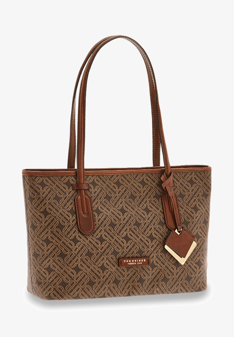 Sac fourre-tout en tissu marron à motifs avec des accents en cuir, doté de deux longues poignées et d'une étiquette décorative. Forme rectangulaire avec une fermeture éclair en haut.