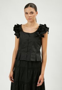 Top peplum negro con mangas con volantes, tejido texturizado y botones en la parte delantera. Combinado con una falda negra con capas. Apariencia general suave.
