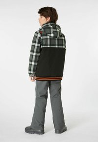 Veste avec un motif à carreaux gris et noir, section inférieure totalement noire, capuche réglable et ourlet à rayures orange ; associée à un pantalon gris.