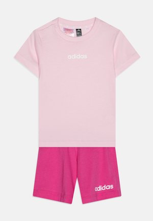 Camiseta de algodón rosa con mangas cortas y logotipo "adidas" en blanco, combinada con pantalones cortos de color rosa brillante que también presentan un logotipo "adidas" en blanco.