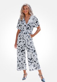 Bloemige jumpsuit in zwart-wit, korte wijde mouwen, v-hals, strikband in de taille, lichtgewicht stof, met een gedurfd bloemenpatroon.