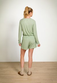 Helle grüne Loungewear-Set besteht aus einem langärmligen Oberteil und Shorts, gefertigt aus einem weichen Stoff mit dezentem geometrischem Muster, elastischem Bund und lockerer Passform.