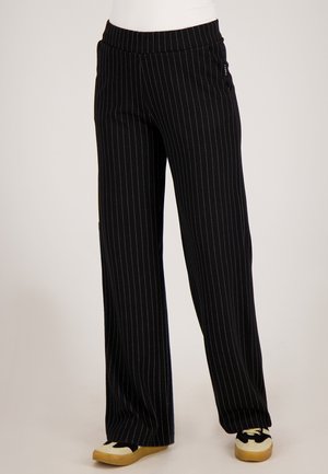 Zwarte broek met krijtstreep en een wijd ontwerp, voorzien van een elastische tailleband en zijzakken, gecombineerd met tweekleurige sneakers.