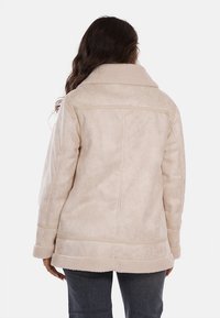 Cappotto in pelliccia ecologica beige con ampio colletto, taglio rilassato e dettagli di cuciture orizzontali, mostrato di spalle. Texture morbida e design di media lunghezza.