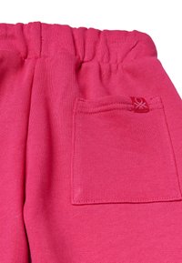 Pantalones de algodón rosa con una cinturilla elástica, que cuentan con un bolsillo trasero y una pequeña etiqueta de logo roja en el lateral. Textura suave, diseño casual.