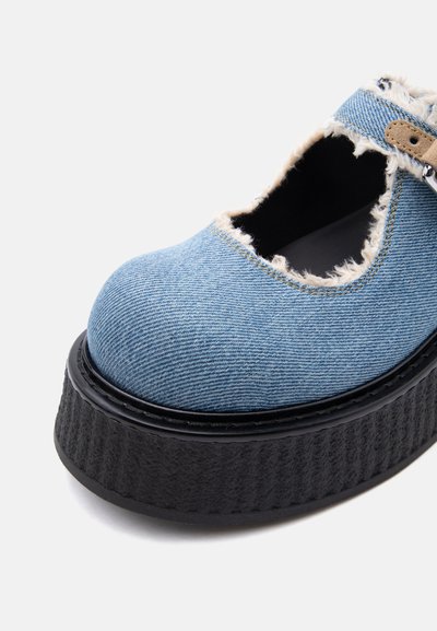 Chaussure à plateforme épaisse avec dessus en denim bleu clair, bords effilochés, semelle noire épaisse et bride marron clair avec fermeture à boucle.