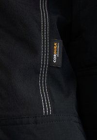 Svart tyg med vit sömnad har en Cordura®-etikett, vilket framhäver hållbart material och avancerad tygteknologi.