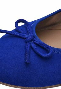 Gros plan sur une ballerine en daim bleu roi avec un nœud noué sur le bout et une doublure intérieure beige.
