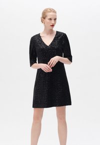 Vestido negro de lentejuelas con escote en V y mangas tres cuartos, que presenta una forma ajustada y un brillo texturizado para un aspecto elegante.