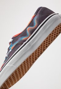 Sneaker in tela nera con motivo arcobaleno ondulato, lacci bianchi, suola bianca e suola in gomma con un motivo a presa testurizzato.