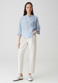 Camicia azzurra chiara a maniche lunghe con colletto rotondo, abbinata a pantaloni bianchi a gamba dritta e sneakers bianche. Tessuto morbido.