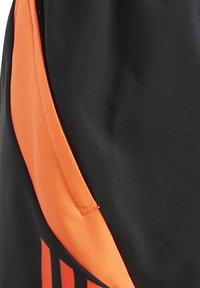 Zwarte sportstof met een oranje paneel en verticale strepen. Glad textuur en ritsdetail aan de zijkant.