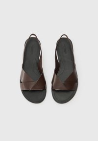Braune Leder-Sandalen mit einem Kreuzriemen-Design, offenem Fersenbereich und flacher Gummisohle, die eine glatte Textur und einen minimalistischen Look aufweisen.