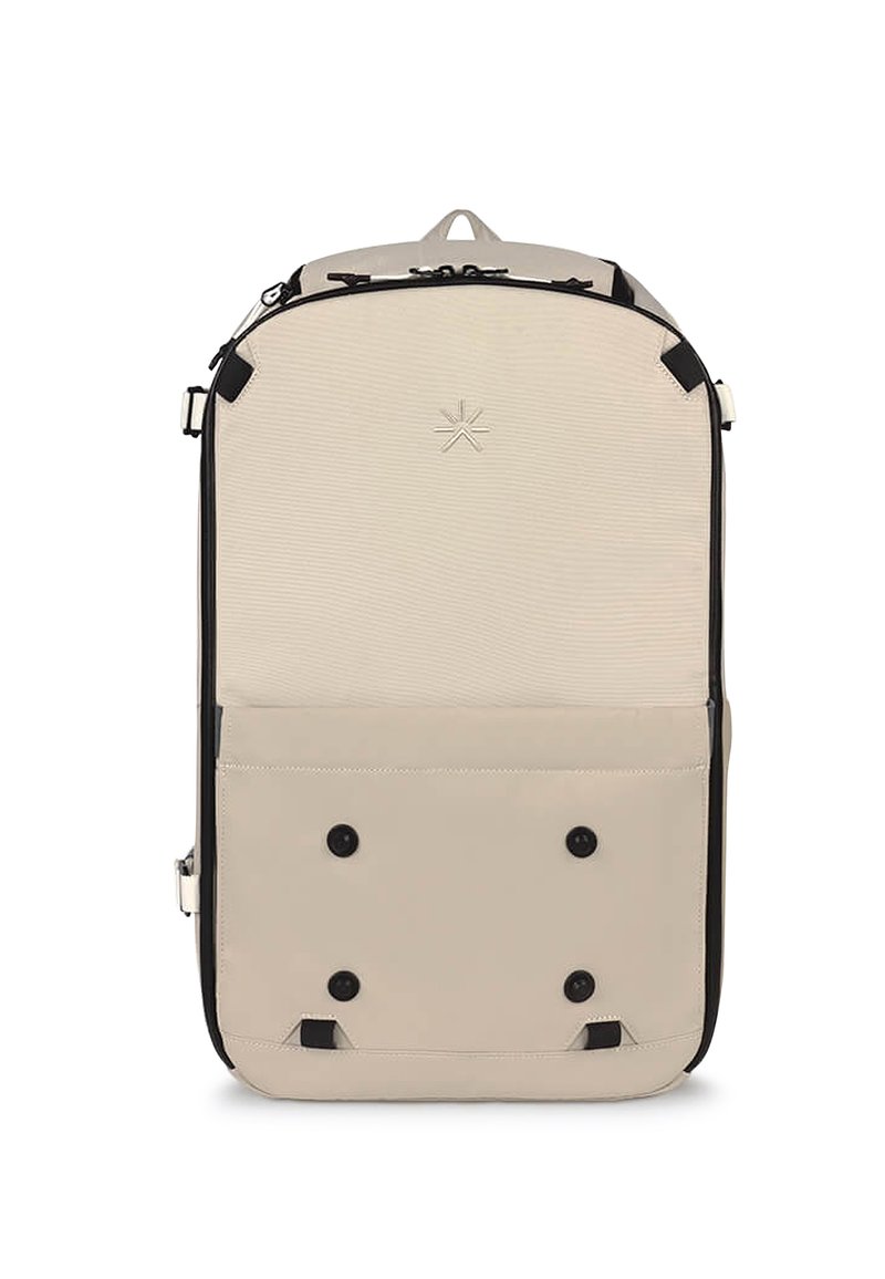 Zaino in tessuto beige con accenti neri. Presenta una chiusura superiore con zip, una tasca frontale con bottoni a pressione e un logo minimalista nella parte anteriore.