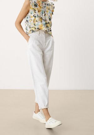 Lehký top bez rukávů s květinovým vzorem, kombinovaný s světle šedými kalhotami a bílými teniskami. Kalhoty mají volný střih a ohrnuté nohavice.