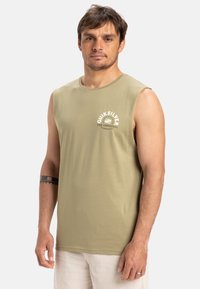 Oližu zaudējošo zaļo bezpiedurkņu T-kreklu ar apļveida apkakli un priekšējo balto logotipa izdruku; izgatavots no mīksta, viegla auduma; gluda tekstūra.