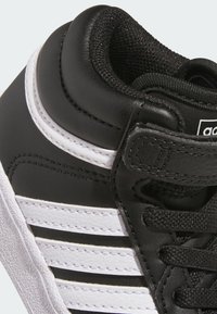 Černé vysoké tenisky s bílými pruhy, vyrobené z syntetické kůže. Mají texturovaný jazyk, kulaté tkaničky a gumovou podrážku.