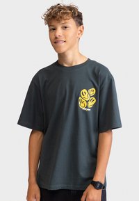 Mörkgrön bomulls t-shirt med korta ärmar, som har gula grafiska smiley-ansikten på vänster bröstområde. Avslappnad passform med rund halsringning.