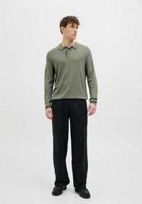 Zāles zaļas piedurknes polo krekls, izgatavots no mīkstas auduma, ar pogu aizdari un ribotu apkakli, apvienots ar melniem platām biksēm.