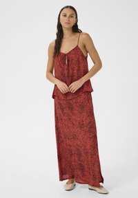 Rode tweedelige outfit bestaande uit een losvallende, mouwloze top met een strikdetail en een bijpassende lange rok, beide met een zwart gespikkeld patroon.