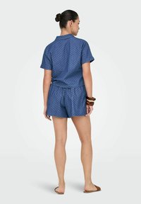 Blå kortärmad skjorta och matchande shorts med ett prickigt mönster. Outfiten har en avslappnad passform och krage.