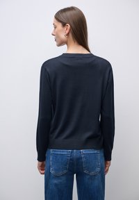 Granatowy sweter z prążkowanym dekoltem i mankietami, o gładkiej fakturze. Noszony z jasnoniebieskimi dżinsami, prezentującymi luźny krój.