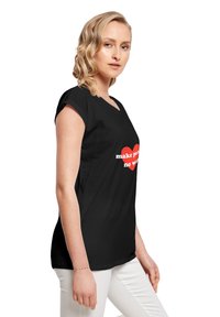 Sort t-shirt med v-hals og korte ærmer. Fronten viser et rødt hjerte grafik med teksten "make peace no war" i hvid. Glat stofstruktur.