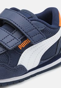 Scarpe da ginnastica Puma con parte superiore in tessuto blu navy, dettagli in pelle bianca, cinturini in Velcro e un dettaglio del logo arancione sul lato.