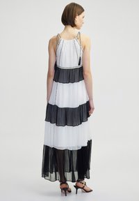 Maxikleid aus geschichtetem schwarz-weißem Chiffon, mit verstellbaren geflochtenen Trägern und gerafftem Saum. Glatte Textur, halbtransparent.