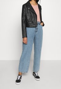 Schwarze kurz geschnittene Lederjacke, hellrosa geripptes Oberteil und weit geschnittene hellblaue Jeans. Schwarz-weiße Sneaker runden das Outfit ab.