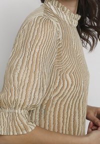 Beige bluse med et bølget stribemønster, høj flæsekrave og elastiske pufærmer, lavet af et let materiale.