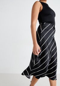 Musta satiinimekko, jossa on istuva yläosa ja pitkä, laskeutuva helma, koristeltuna valkoisilla vinoraitakuoseilla. Sileä pinta ja kevyt kiilto.