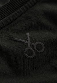 Zwarte gebreide stof met een zwart schaar graphic. Het ontwerp is eenvoudig met een subtiele glans en geribbelde randen.