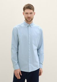Light blue button-up shirt with long sleeves, a collared neck, a chest pocket, and subtle texture; fabric appears soft and slightly shiny.