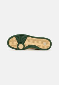 Suola di una sneaker con un fondo in gomma verde, caratterizzato da un motivo zigzag testurizzato e un accento circolare beige. Nome del marchio visibile.